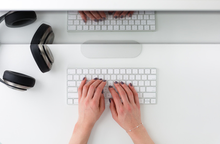 Workplace with a womans hands typing on a keyboard shot from above