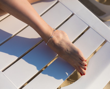 Closeup of a woman's legs with an anklet jewelry on the beach