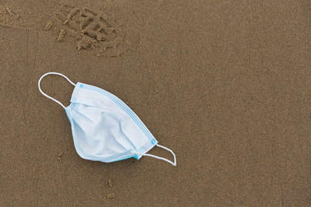 Used surgical face mask laying on a beach