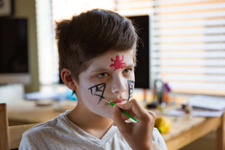 Boy with a face paint decorating spooky Halloween cupcakesの写真素材