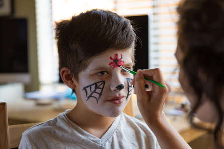 Boy with a face paint decorating spooky Halloween cupcakesの写真素材