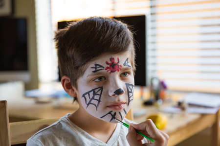 Boy with a face paint decorating spooky Halloween cupcakesの写真素材