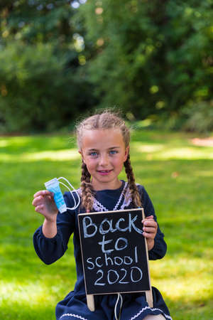 Schoolgirl holding a back to school sign and a face maskの写真素材