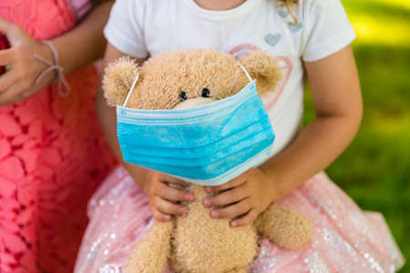 Girl holding a teddy bear with a surgical maskの写真素材