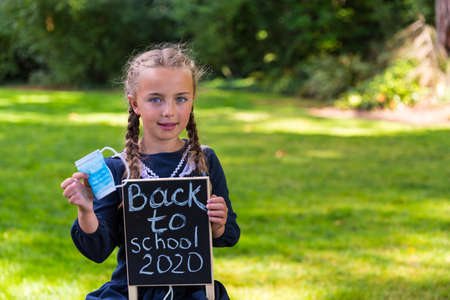 Schoolgirl holding a back to school sign and a face maskの写真素材
