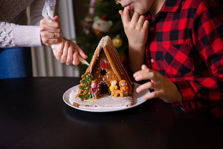 A boy decorating Christmas gingerbread house  at homeの写真素材