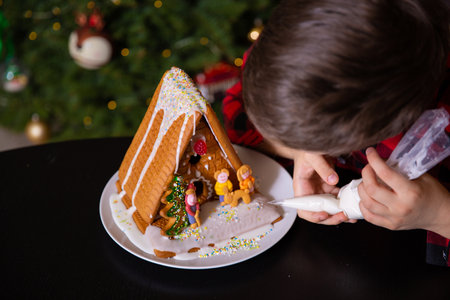 A boy decorating Christmas gingerbread house  at homeの写真素材