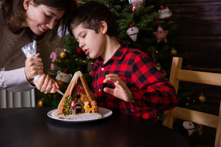A boy decorating Christmas gingerbread house  at homeの写真素材