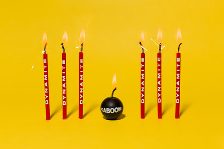 Red dynamite birthday candles burning on a bright yellow background