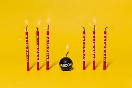 Red dynamite birthday candles burning on a bright yellow backgroundの写真素材