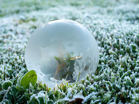 World globe on a meadow with frost in winter