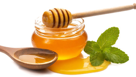 jar of honey with wooden spoon on white backgroundの素材