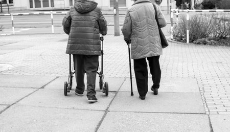 Two old women on a street with a walker and a walking stick black and white photographyの写真素材