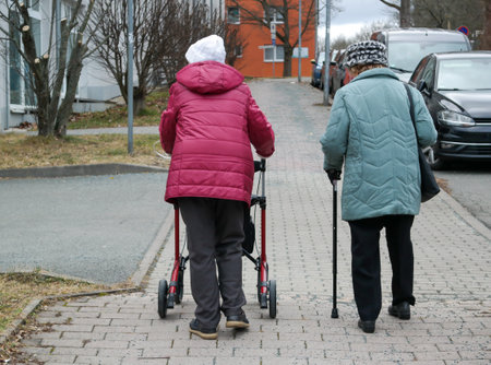 Two old women on a street with a walker and a walking stickの写真素材