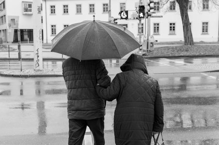 Pensioner couple walking in the rain at a traffic light in the city of black and white photographyの写真素材