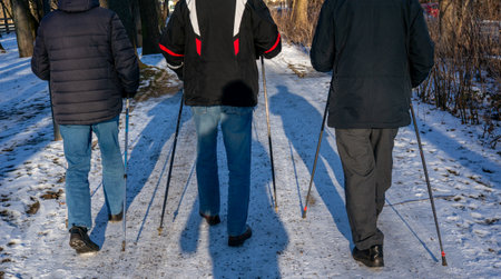 old man doing Nordic walking in a park in winter with snow on the wayの写真素材
