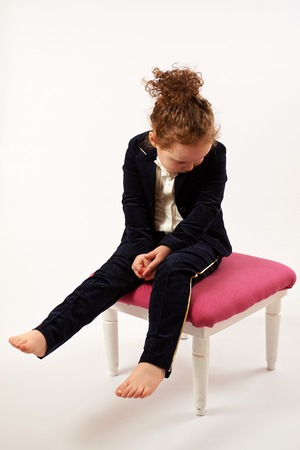 Little girl in black suit sitting and poutingの写真素材