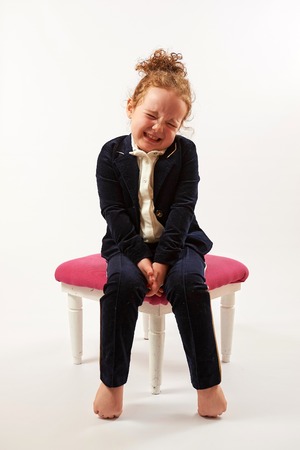 Little girl in black suit sitting on a rose stoolの写真素材