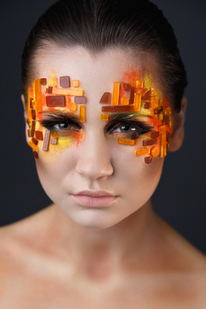 Portrait of a girl with an original make-up. Beauty close-up. Orange and red rhinestones on a faceの写真素材