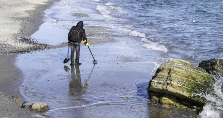 ODESSA, UKRAINE - 01.25.2017. Man with metal detector looking for treasure on the beach in a early winter morning.のeditorial素材