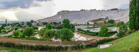 Pamukkale, Turkey â 07.14.2019. White mountain and green lake in Pamukkale. Panoramic view from the side of the village on a cloudy summer evening.のeditorial素材