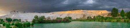Pamukkale, Turkey â 07.14.2019. White mountain and green lake in Pamukkale. Panoramic view from the side of the village on a cloudy summer evening.のeditorial素材