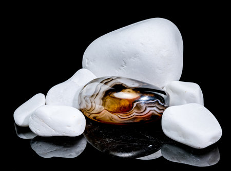 A polished agate stone with rich brown and white bands sits among a collection of smooth, white pebblesの写真素材