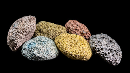 A horizontal studio shot featuring a variety of porous volcanic rocks in different colors. The...