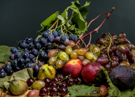 A detailed close-up still life featuring an assortment of fresh fruits, including various colored grapes, peaches, dark figs, and cherries, on a dark backgroundの写真素材