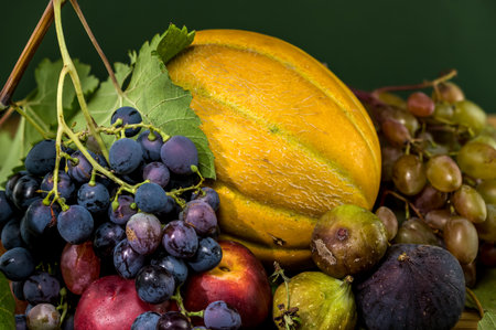 A vibrant still life of various fruits, including fresh grapes, a golden melon, ripe peaches, dark figs, and glossy cherries, arranged on a rustic wooden tableの写真素材