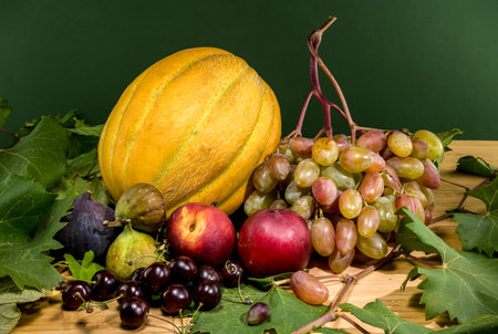 A vibrant still life of various fruits, including fresh grapes, a golden melon, ripe peaches, dark figs, and glossy cherries, arranged on a rustic wooden tableの写真素材