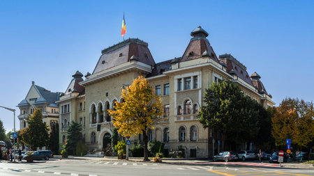 Targu Mures, Romania - October 17.2025. A street view in the historic center of Targu Mures, Romania, featuring ornate buildings, street parking, traffic, and autumn trees under a bright blue skyのeditorial素材