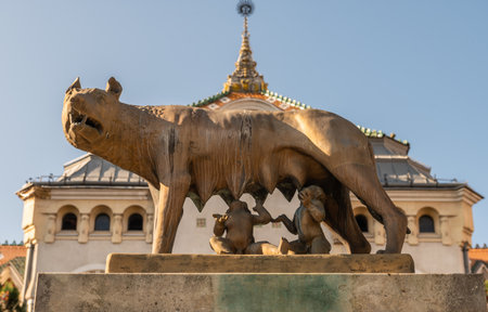 Targu Mures, Romania - October 17.2025. the bronze Lupa Capitolina Capitoline Wolf statue, depicting the legendary she-wolf suckling Romulus and Remus, with the ornate Art Nouveau facade and spire of the Cultural Palaceのeditorial素材