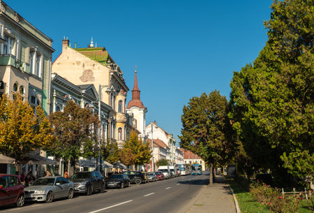 Targu Mures, Romania - October 17.2025. A street view in the historic center of Targu Mures, Romania, featuring ornate buildings, street parking, traffic, and autumn trees under a bright blue skyのeditorial素材