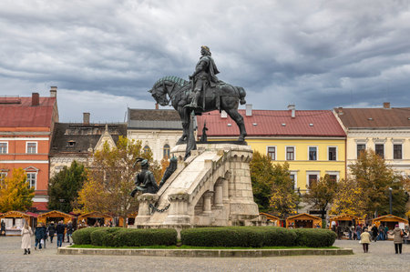 Cluj-Napoca, Romania - October 18.2025. the Matthias Corvinus Monument and surrounding historic buildings in Union Square, featuring a public exhibition and autumn trees under a cloudy skyのeditorial素材