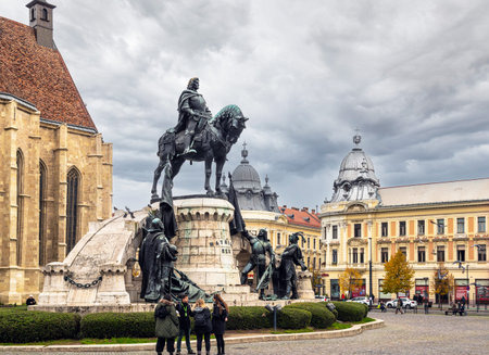 Cluj-Napoca, Romania - October 18.2025. the Matthias Corvinus Monument and surrounding historic buildings in Union Square, featuring a public exhibition and autumn trees under a cloudy skyのeditorial素材