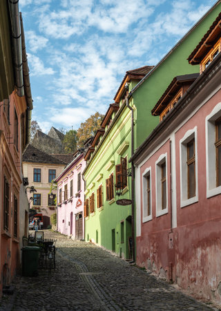 Sighisoara, Romania - 10/21/2025. A charming view of vibrant pink, green, and orange historic houses lining a narrow uphill cobblestone alleyway in the UNESCO medieval citadel of Sighisoaraのeditorial素材