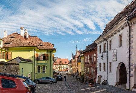 SighiÈoara, Romania - 10/21/2025. A lively view of historic lime green and yellow buildings along a cobblestone street featuring an outdoor restaurant and festive bunting in SighiÈoara Romania.のeditorial素材