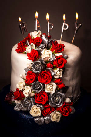 Birthday cake with red and white roses and candles on dark background