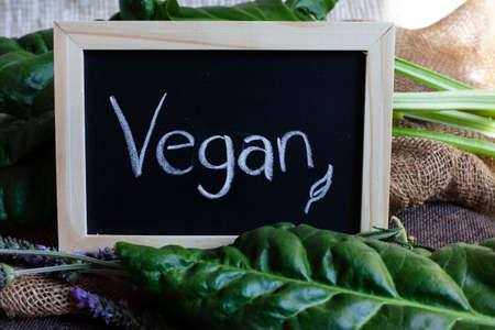 chalkboard with fresh green leafy vegetables with the word vegan written downの写真素材