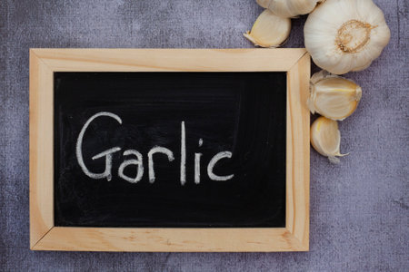 the word garlic written on black chalkboard with garlic cloves on rustic surfaceの写真素材