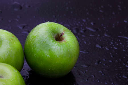 fresh and crisp green granny smith apples on black surface with water dropletsの写真素材