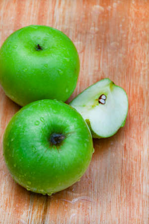 fresh and crisp green granny smith apples on wooden surface with water droplets