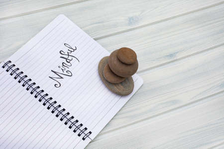 Notebook with the word mindful written on it. Placed on a  pastel wooden grain with beach feel