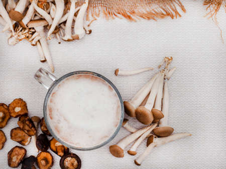 flat lay of mushroom latte in glass mug surrounded with various mushrooms on rustic surfaceの写真素材