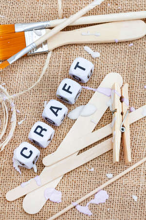 rustic hessian surface with neutral colored art supplies and pastel colored paint splatter with the word Craft in letter dice and ample copy spaceの写真素材
