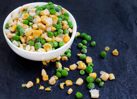 Frozen green garden peas covered in ice on black surface with selective focusの写真素材