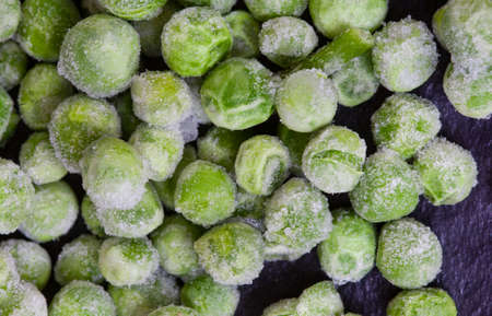 Frozen green garden peas covered in ice on black surface with selective focusの写真素材