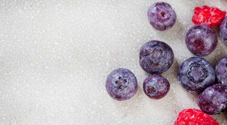 Frozen blueberries and raspberries with water droplets on light grey with copy space
