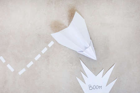 Paper airplane as metaphor, heading for a crash or explosion, on grey with copy spaceの写真素材